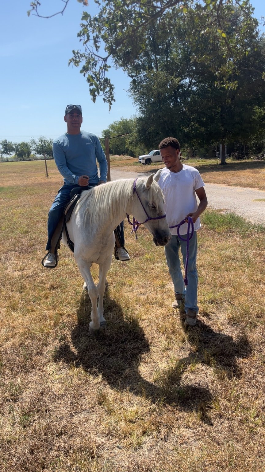 A rider on a white horse guided by a ranch team member